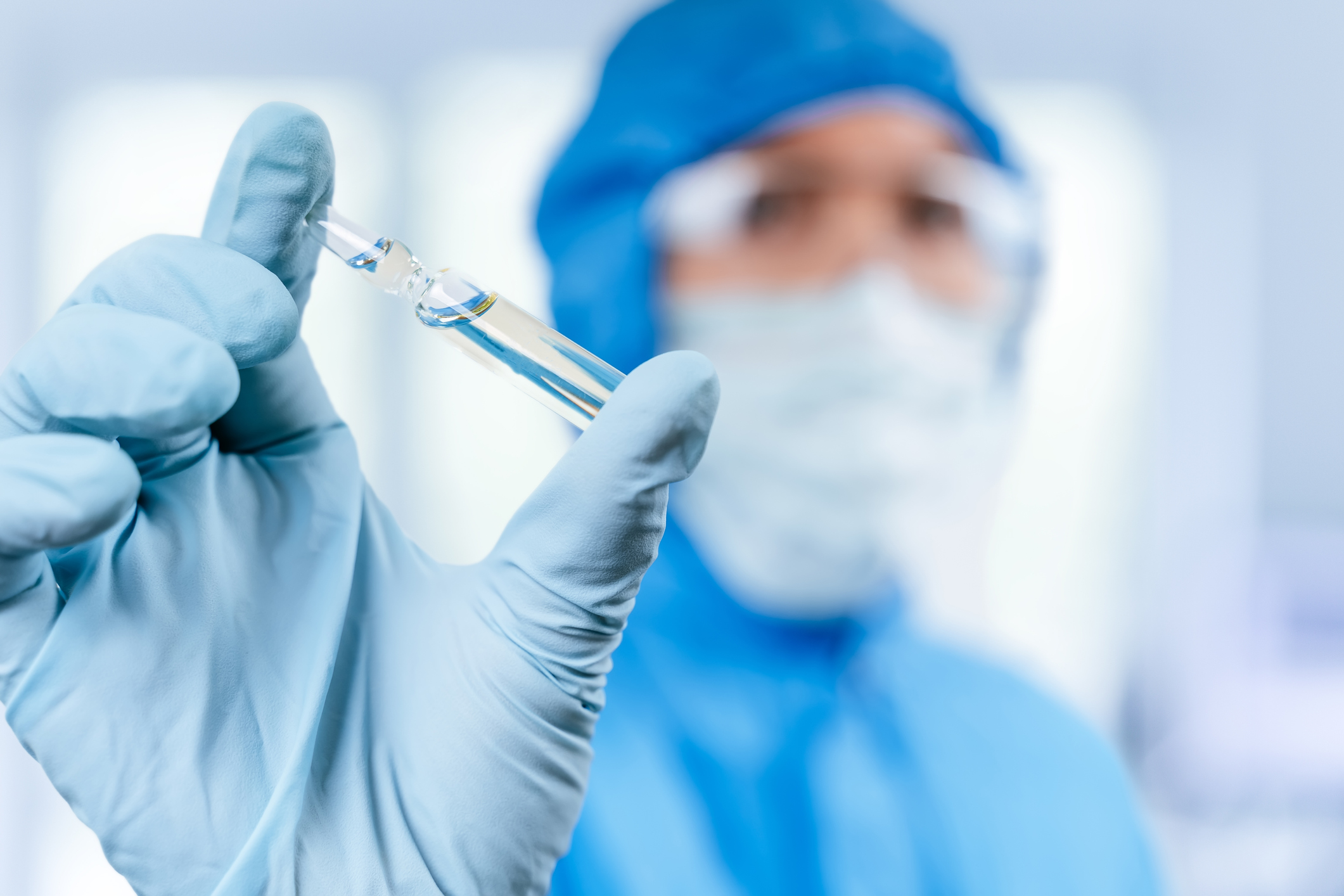 A person wearing safety gear holding a liquid-filled vile. 