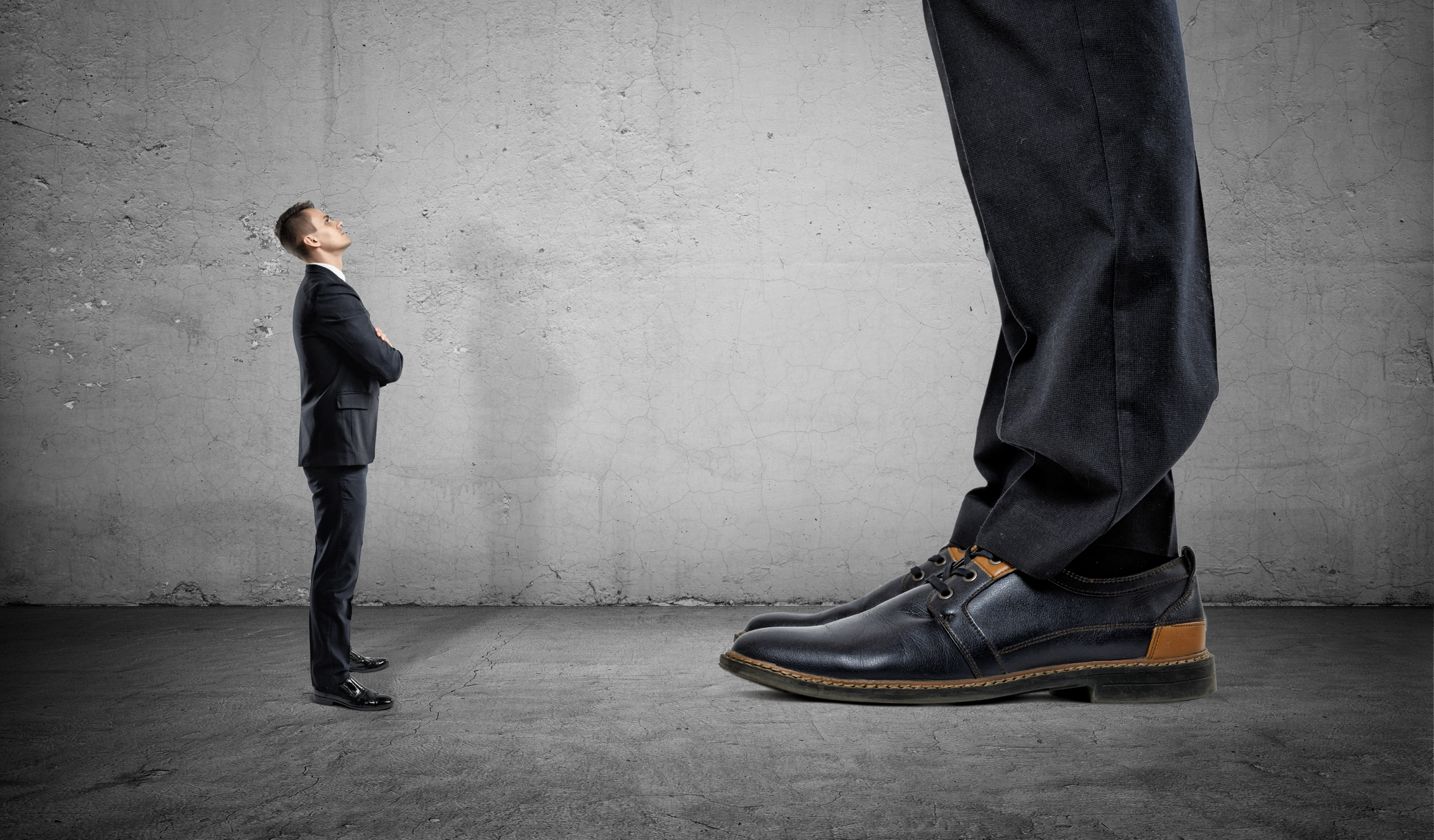 A small businessman looks upwards at a giant businessman whose shoes and pants are only seen in the frame.