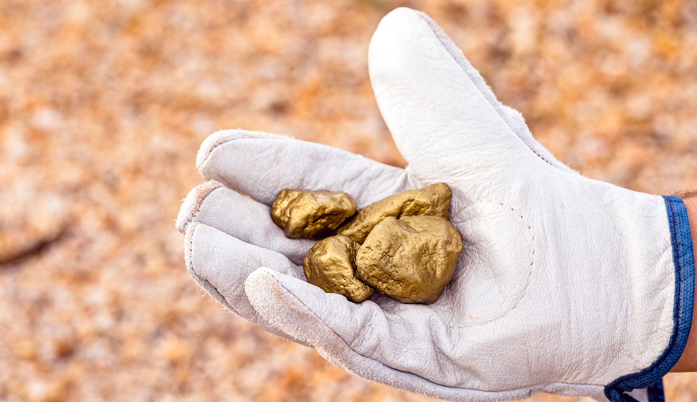 A miner's gloved hand holds gold nuggets.