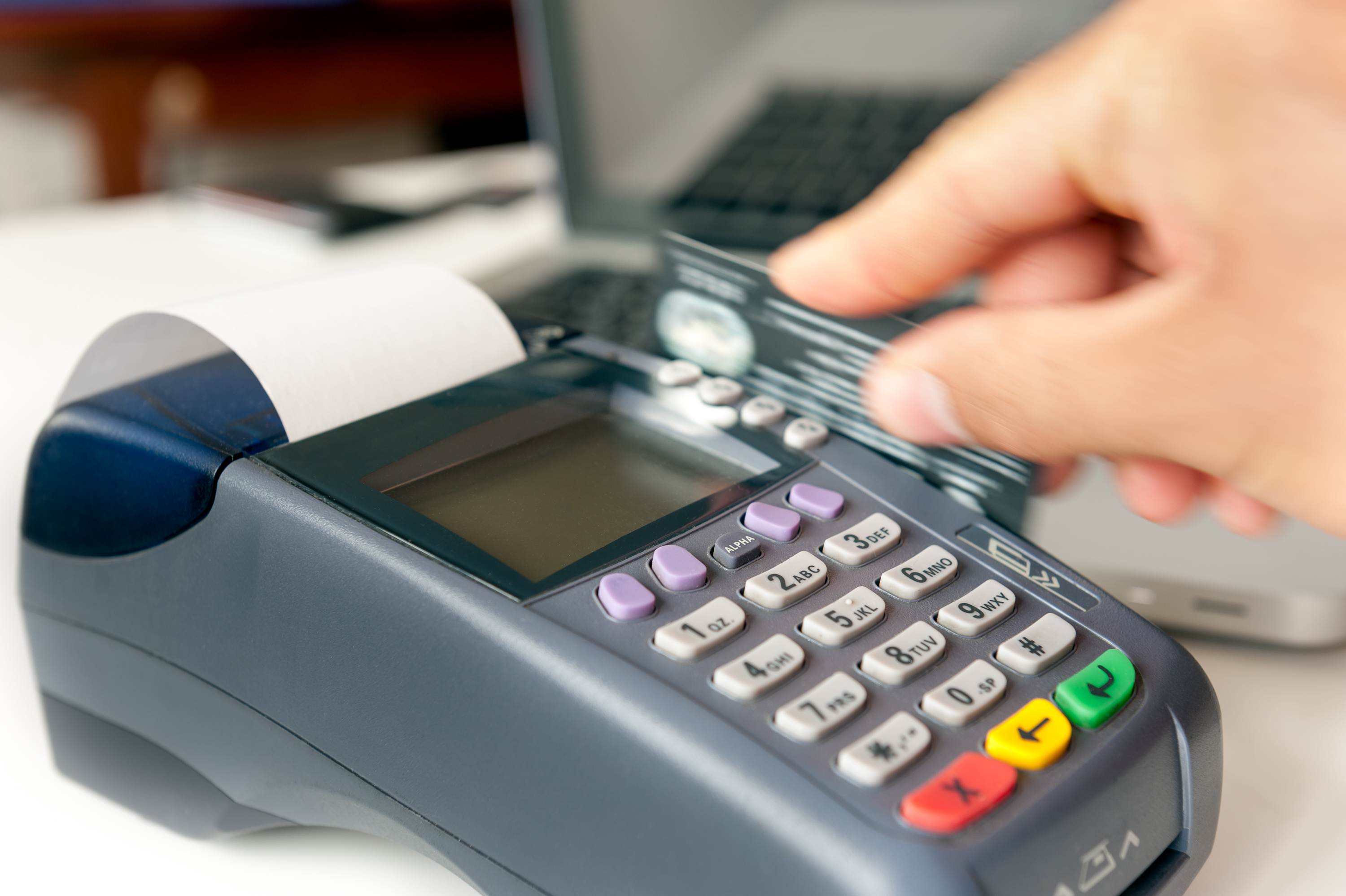 A hand swiping a credit card through a credit card machine