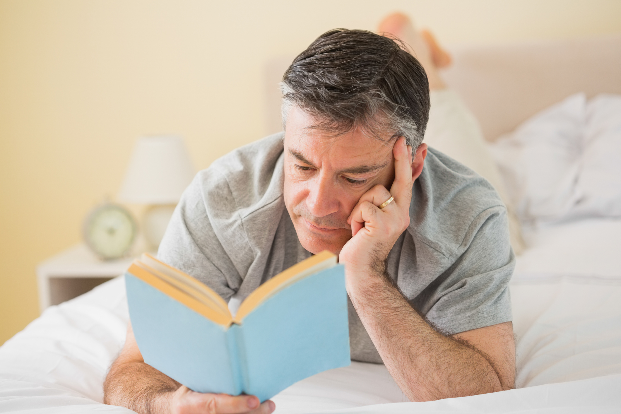 Older man reading book lying in bed