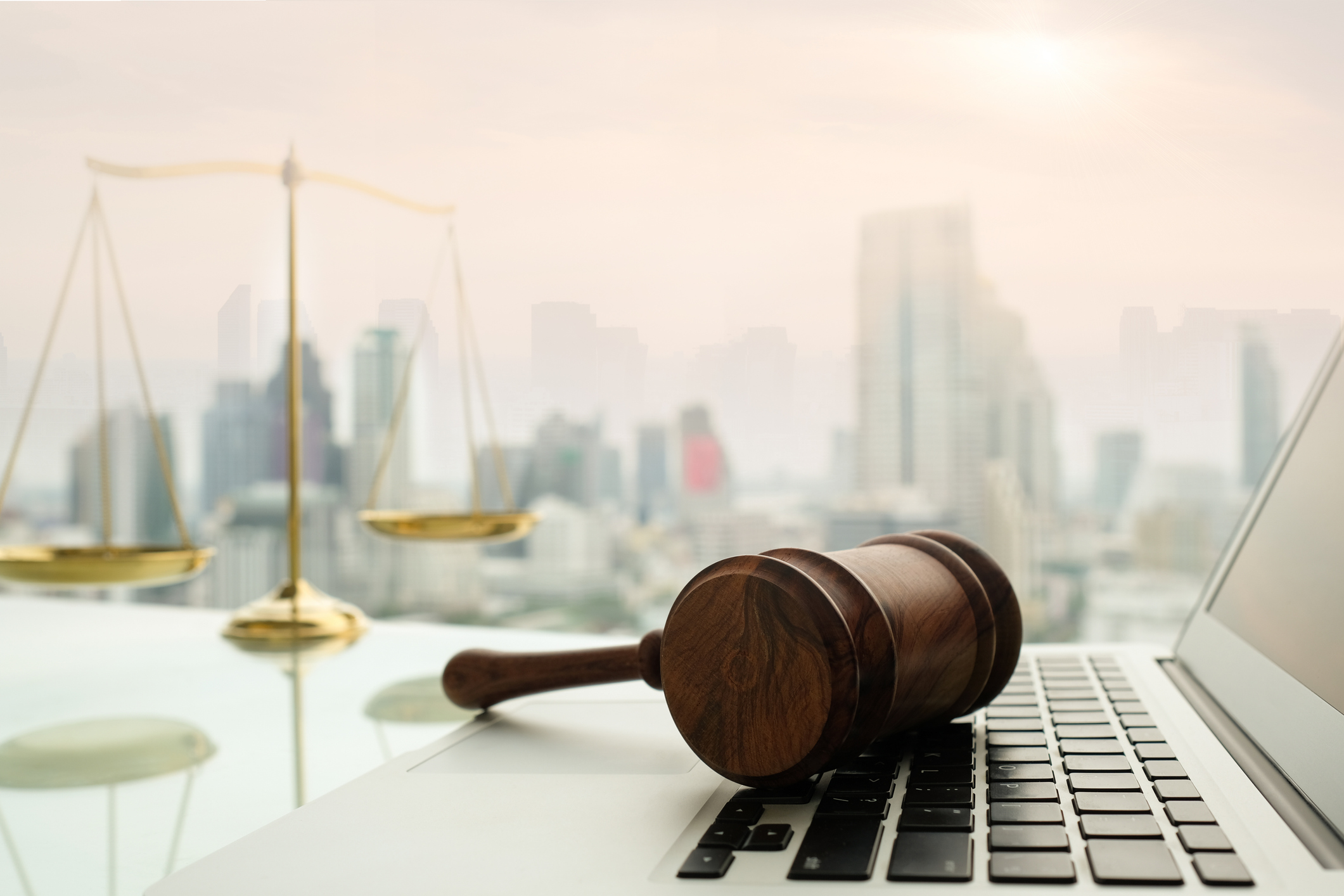Gavel on laptop with scales of justice in the background against a cityscape.