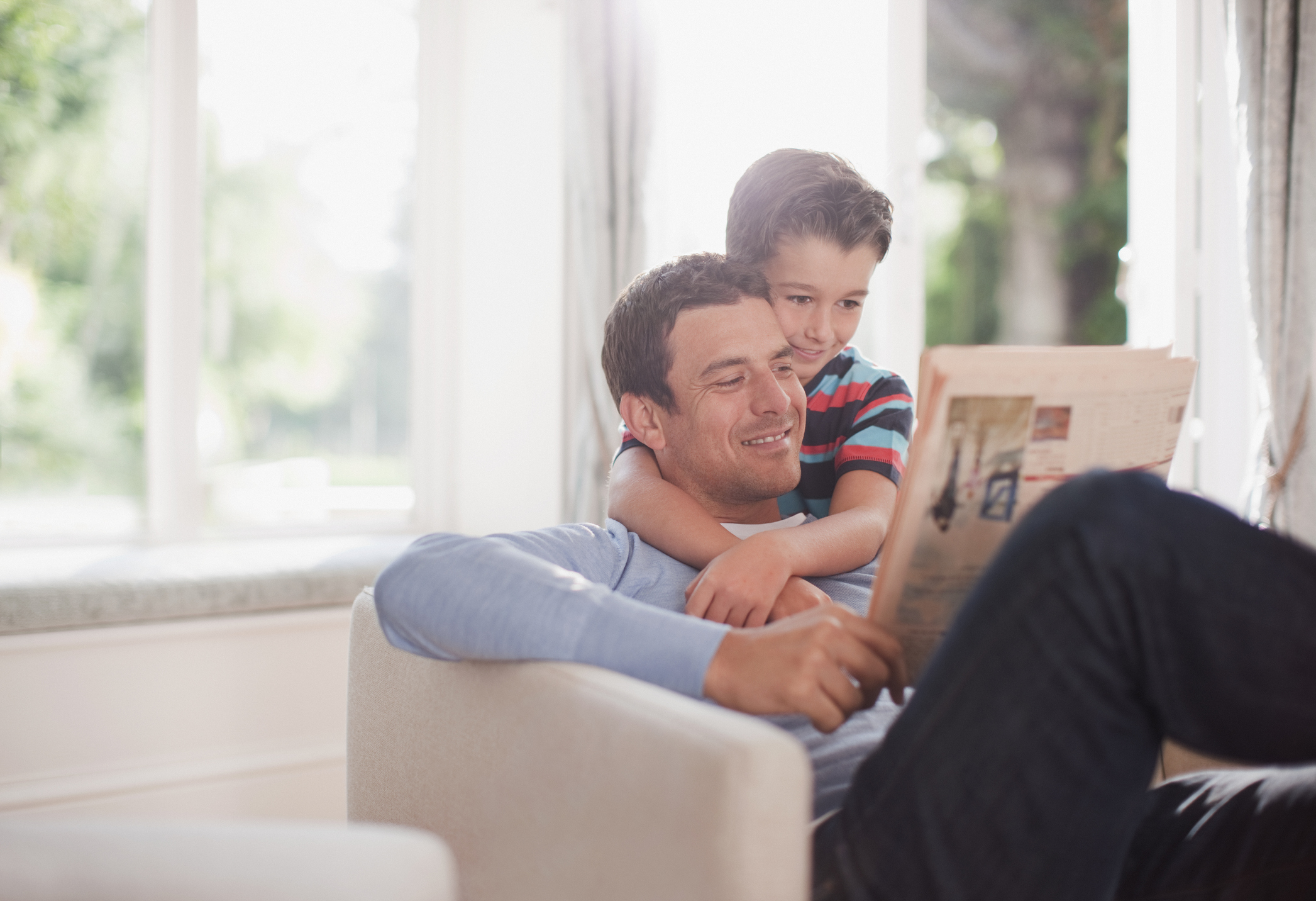 Man in armchair reading newspaper being hugged by young boy