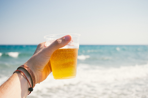 A hand holding a cup of beer on a beach