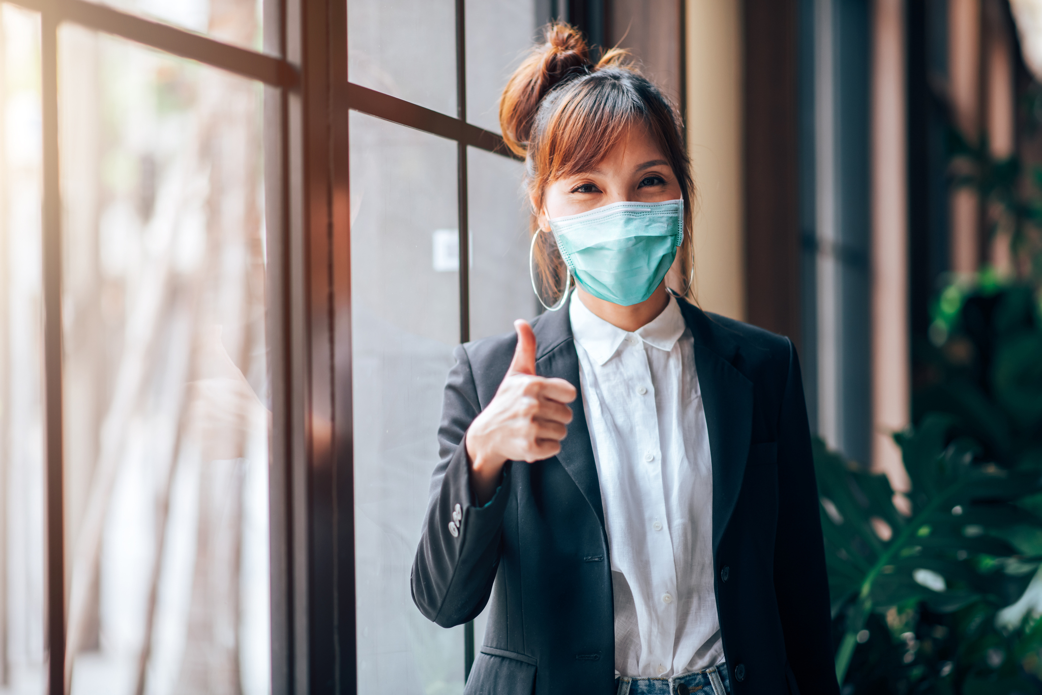 A young woman wears a face mask and gives a thumbs-up.