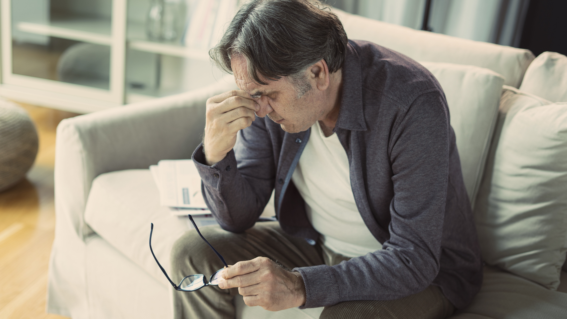 Older man sitting on couch pinching his nose