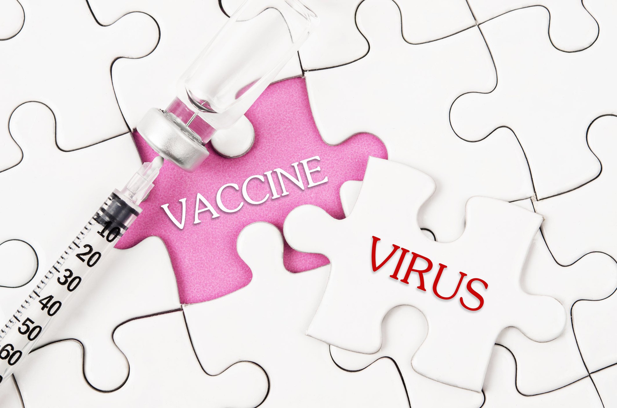 A syringe resting next to a jig saw puzzle piece displaying the word vaccine.