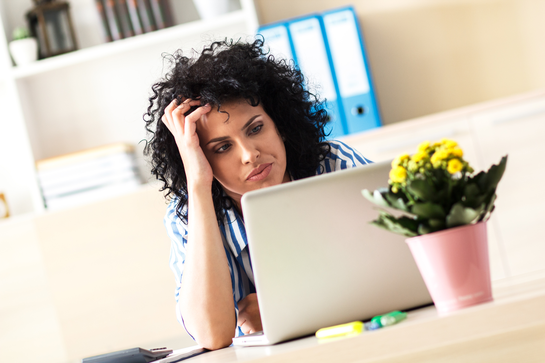 A visibly frustrated woman looking at her laptop, with her hand on her forehead.