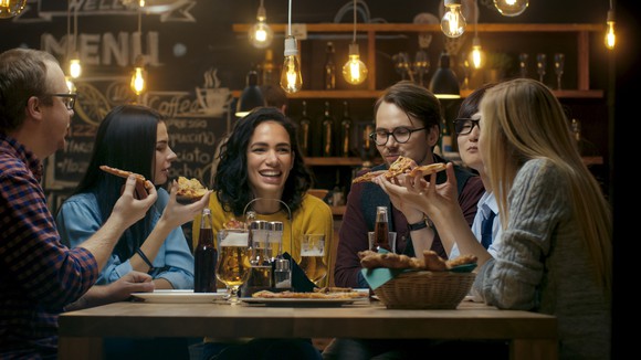 A group of young people eating pizza around a restaurant table