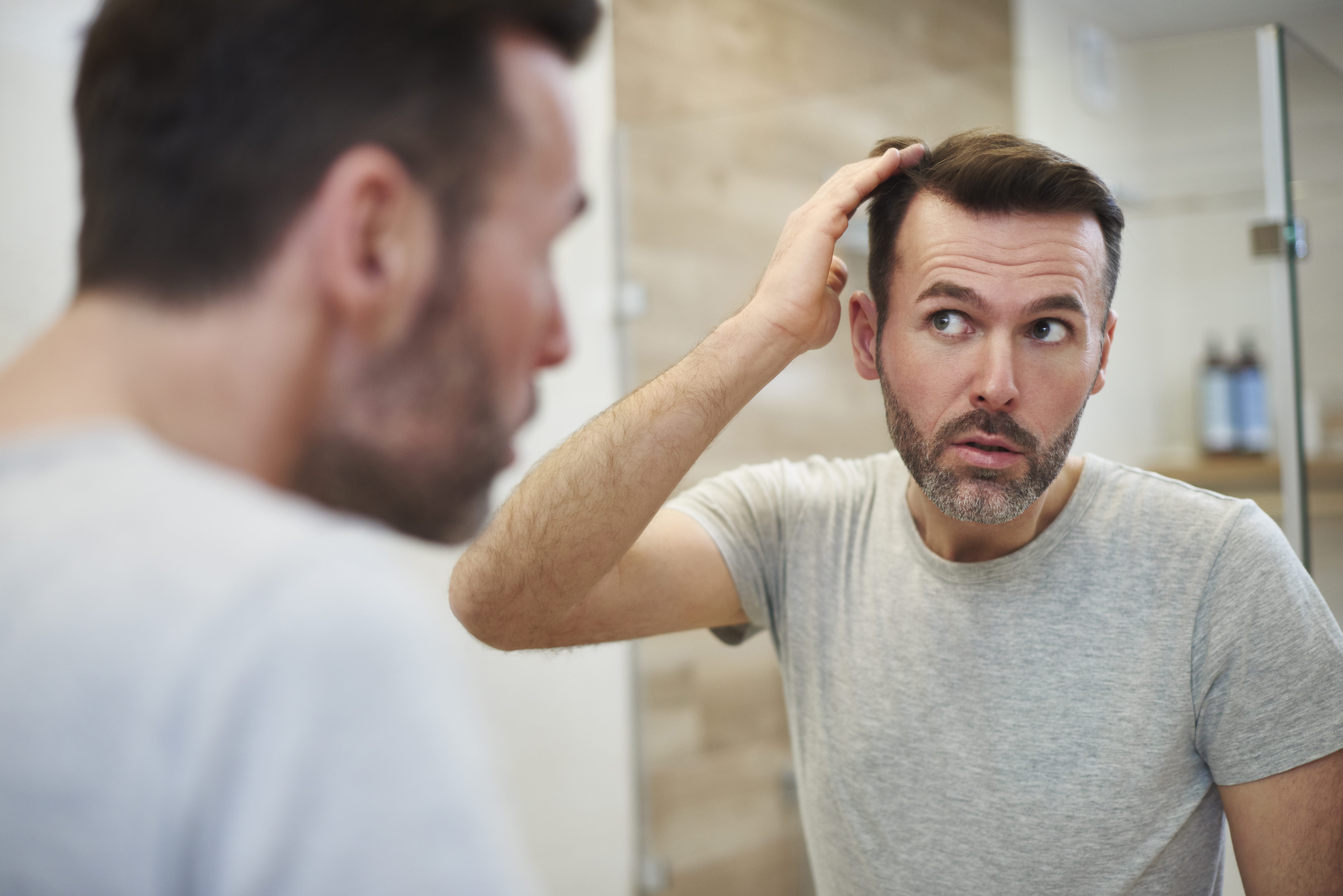 A man checks his hair in the mirror.