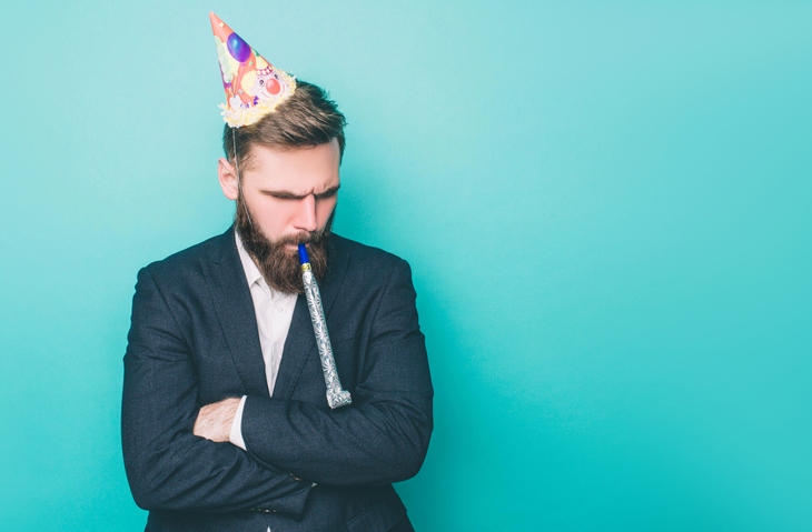 A man in a suit wearing a party hat and blowing a noisemaker