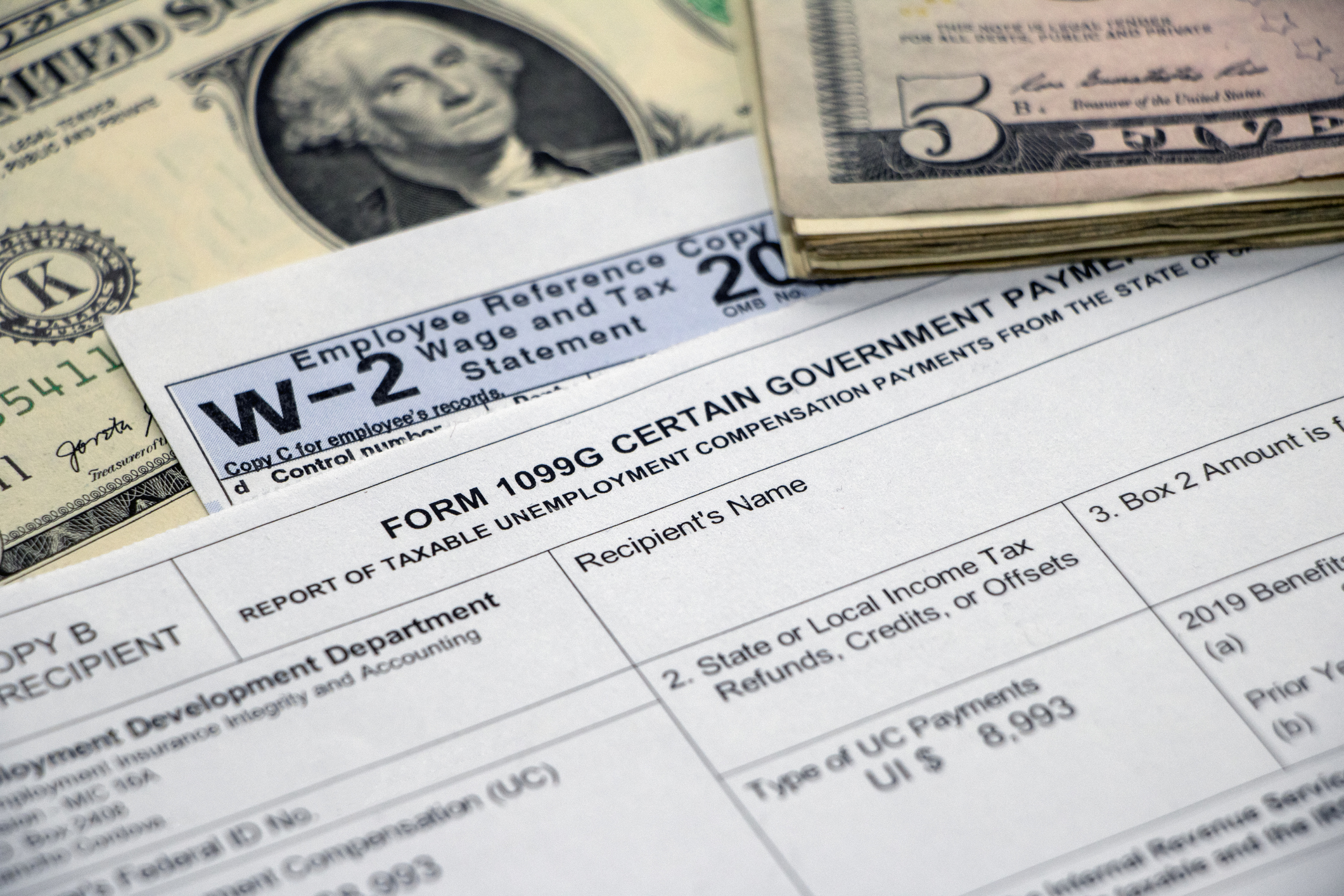 A 1099G unemployment benefits tax form and W2 next to cash.
