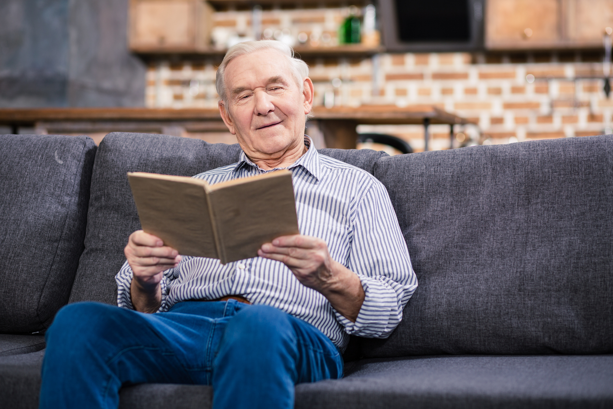 Older man sitting on a couch, reading a book