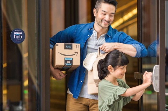 A man carrying an Amazon package under his arm, with his daughter opening the door. 