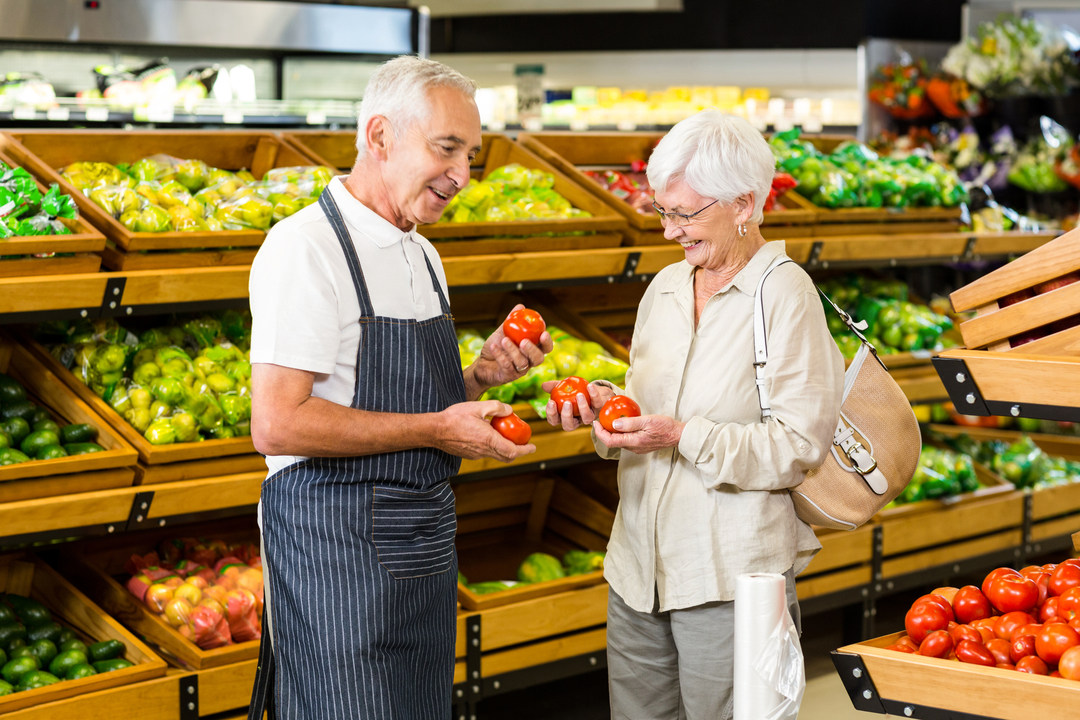Older man in apron and older woman in supermarket holding tomatoes