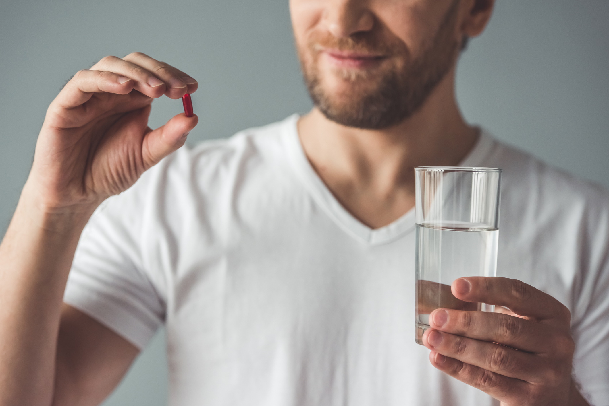 Man holding pill in one hand and glass of water in other hand