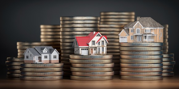 Miniature homes on top of rising stacks of gold coins.