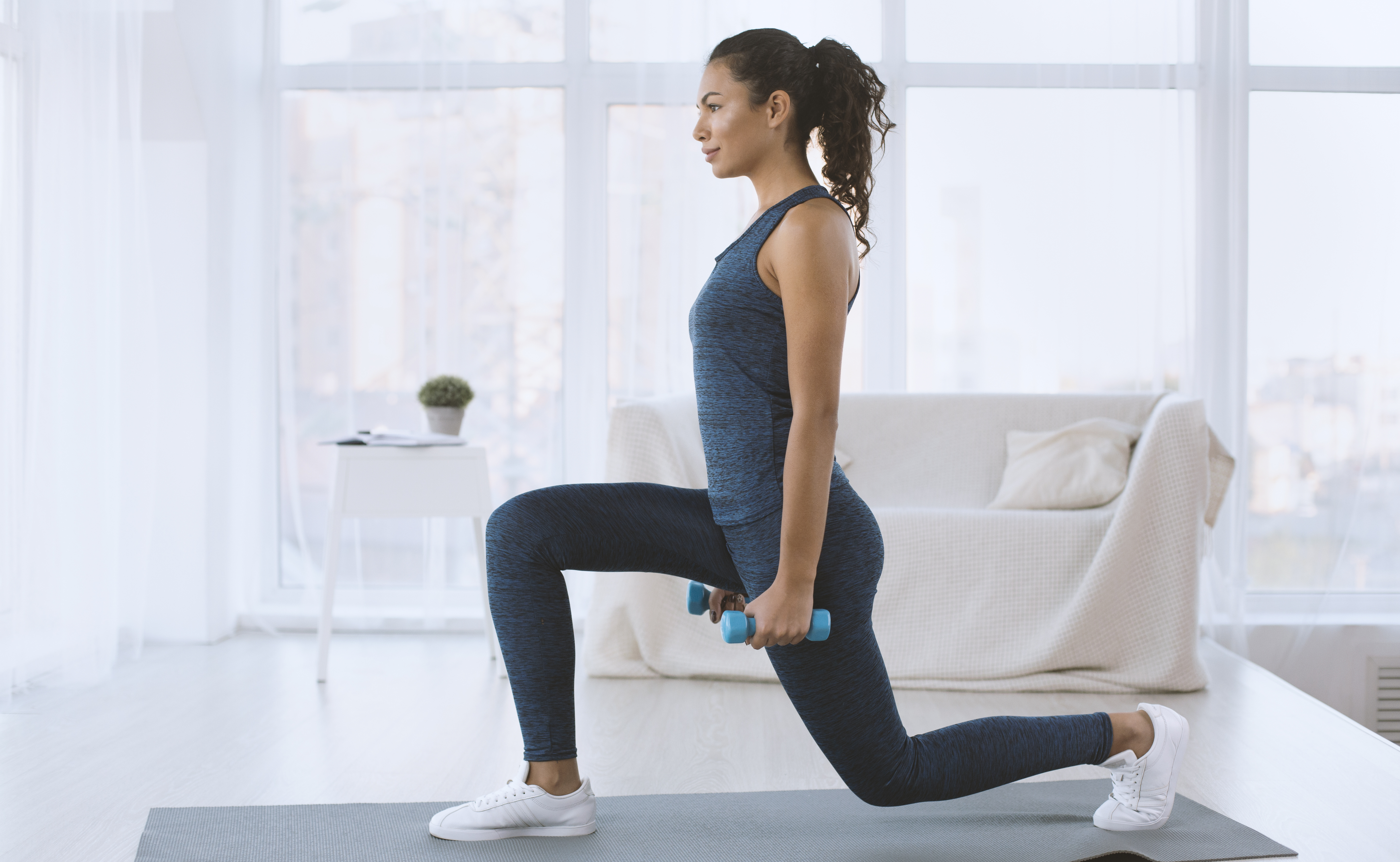 Woman doing lunges with hand weights at home.