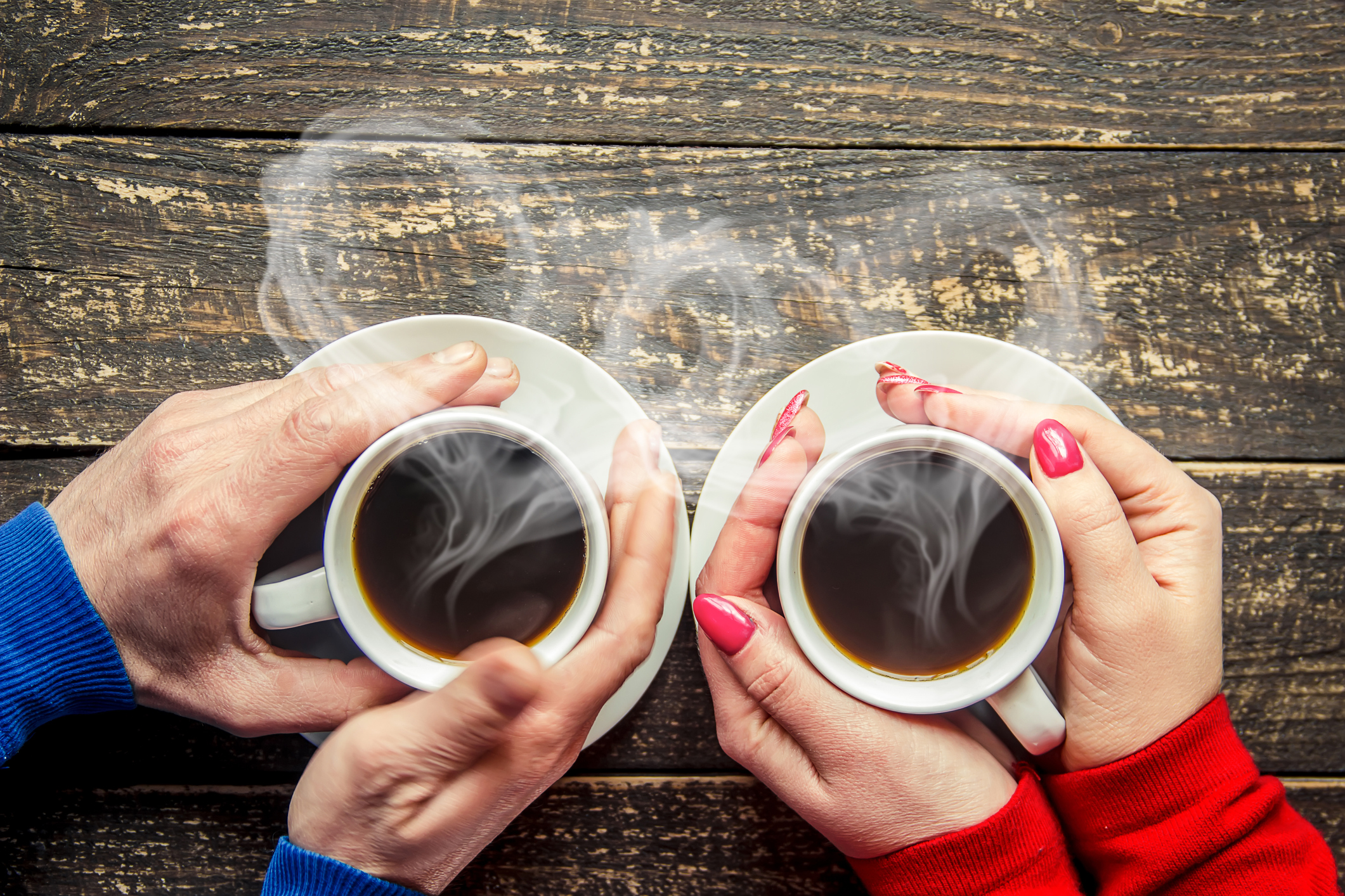 Two people each enjoying a coffee with heart-shaped steam rising from the mugs.