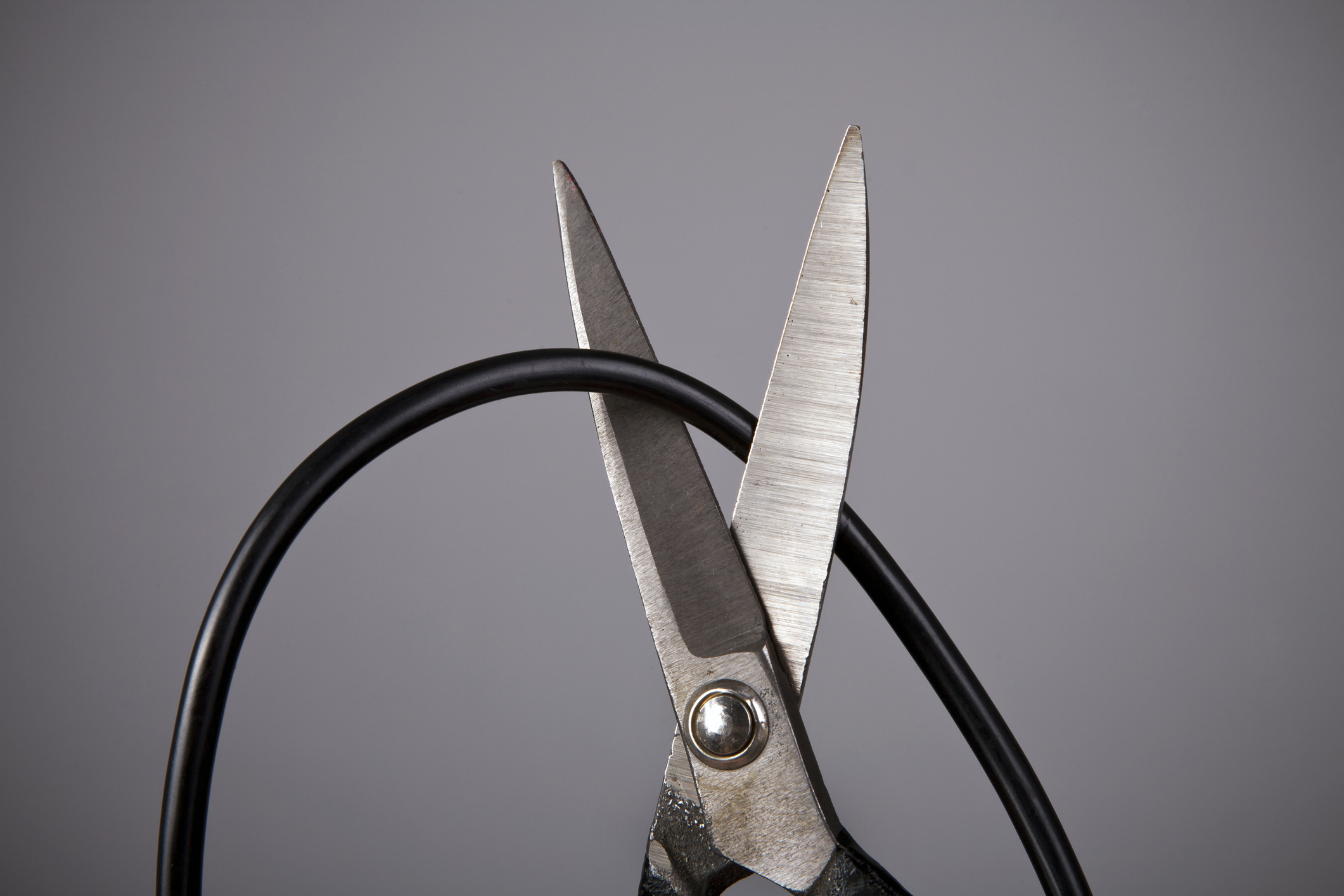 A pair of scissors cutting through a coaxial cable cord