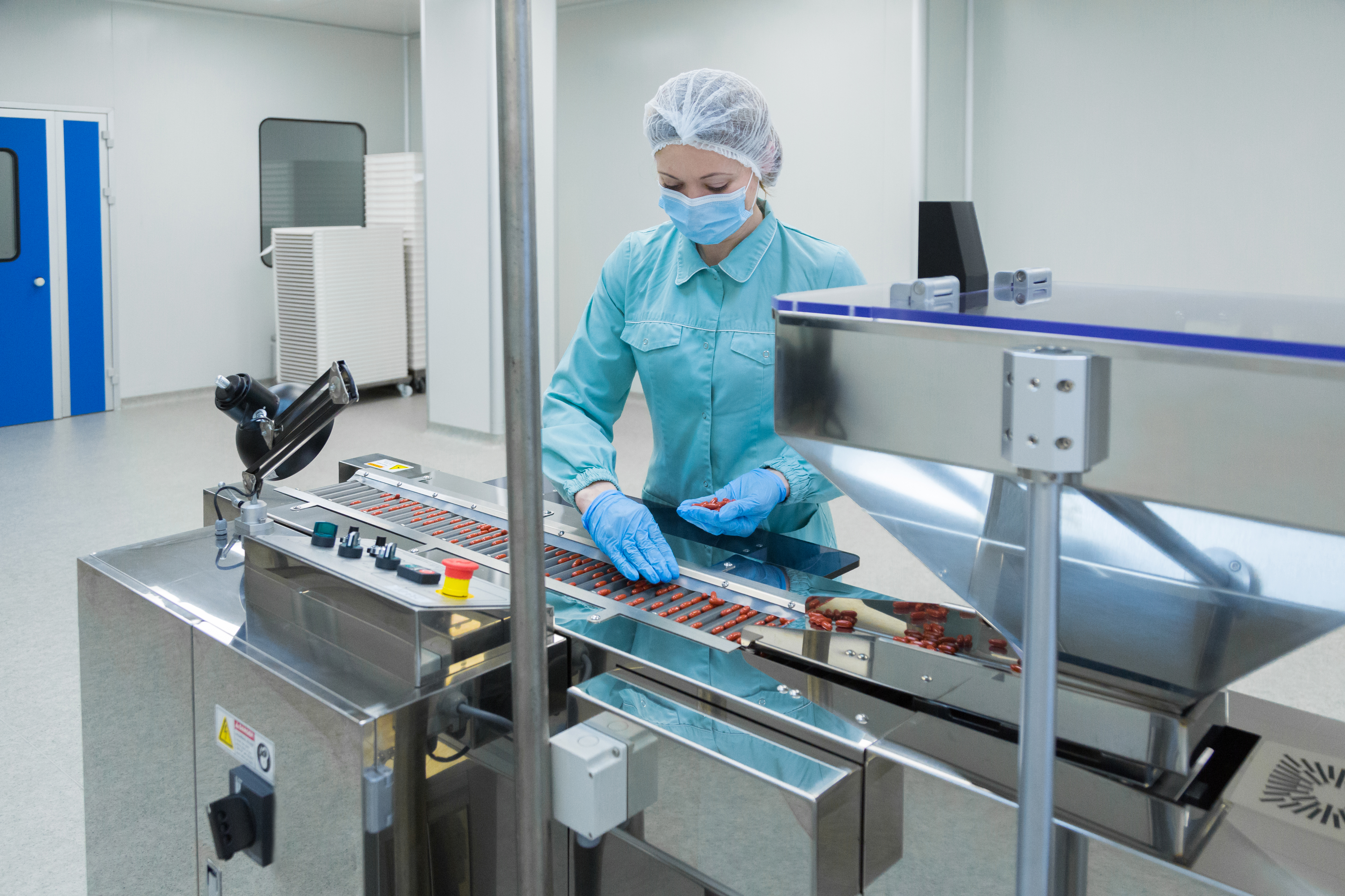 Pharmaceutical technician in sanitized environment working on production of pills at pharmacy factory.