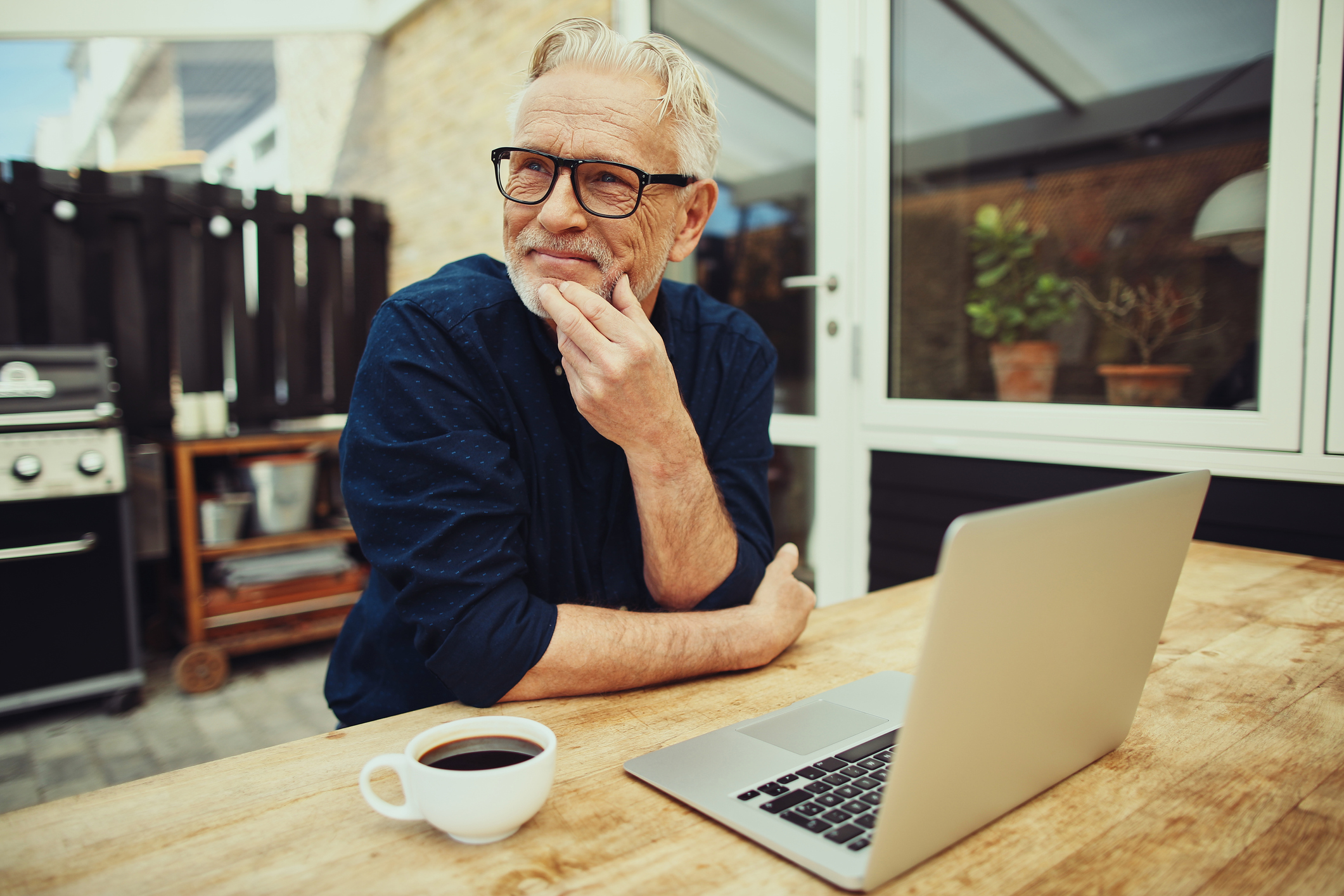 Smiling older man at table with laptop and mug of coffee
