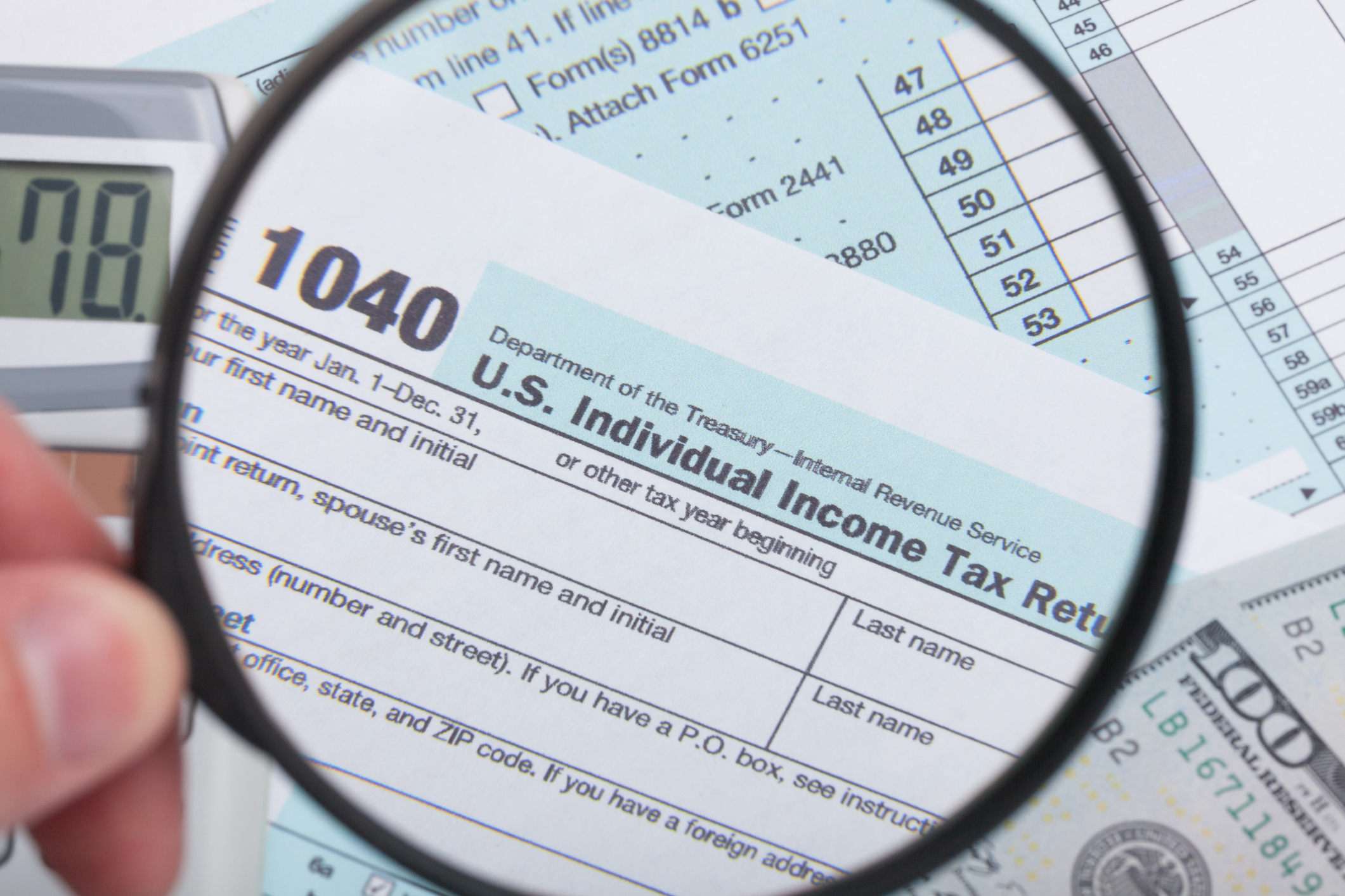 A person holding a magnifying glass above an IRS 1040 tax form.
