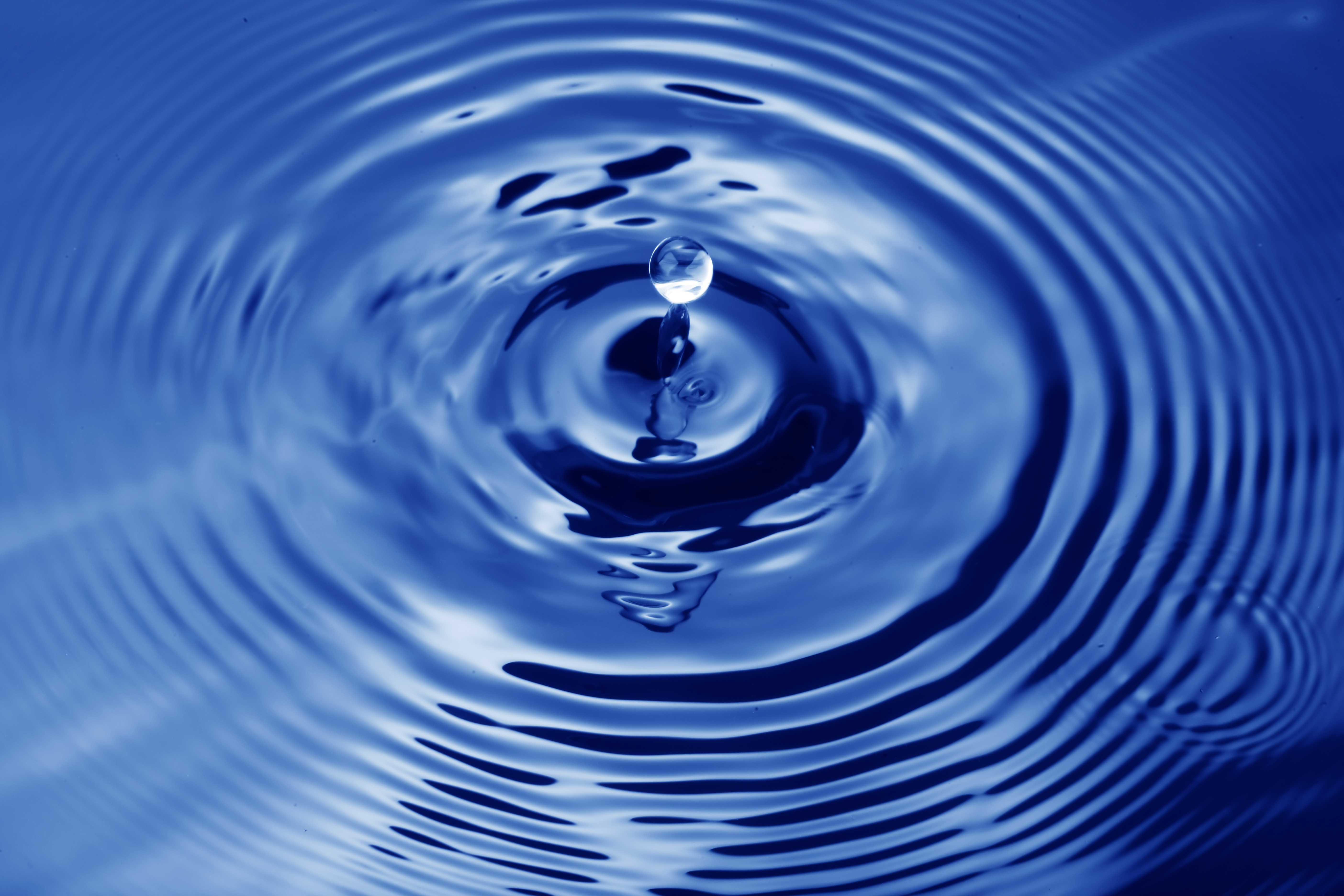 Drop of water falling into a deep blue body of water causing ripples.
