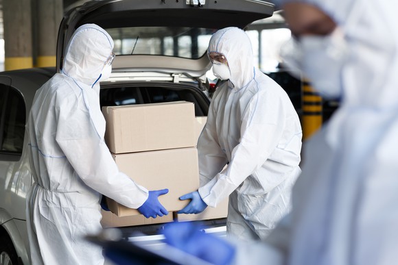 A group of delivery workers delivers some packages while wearing face masks and protective clothing.