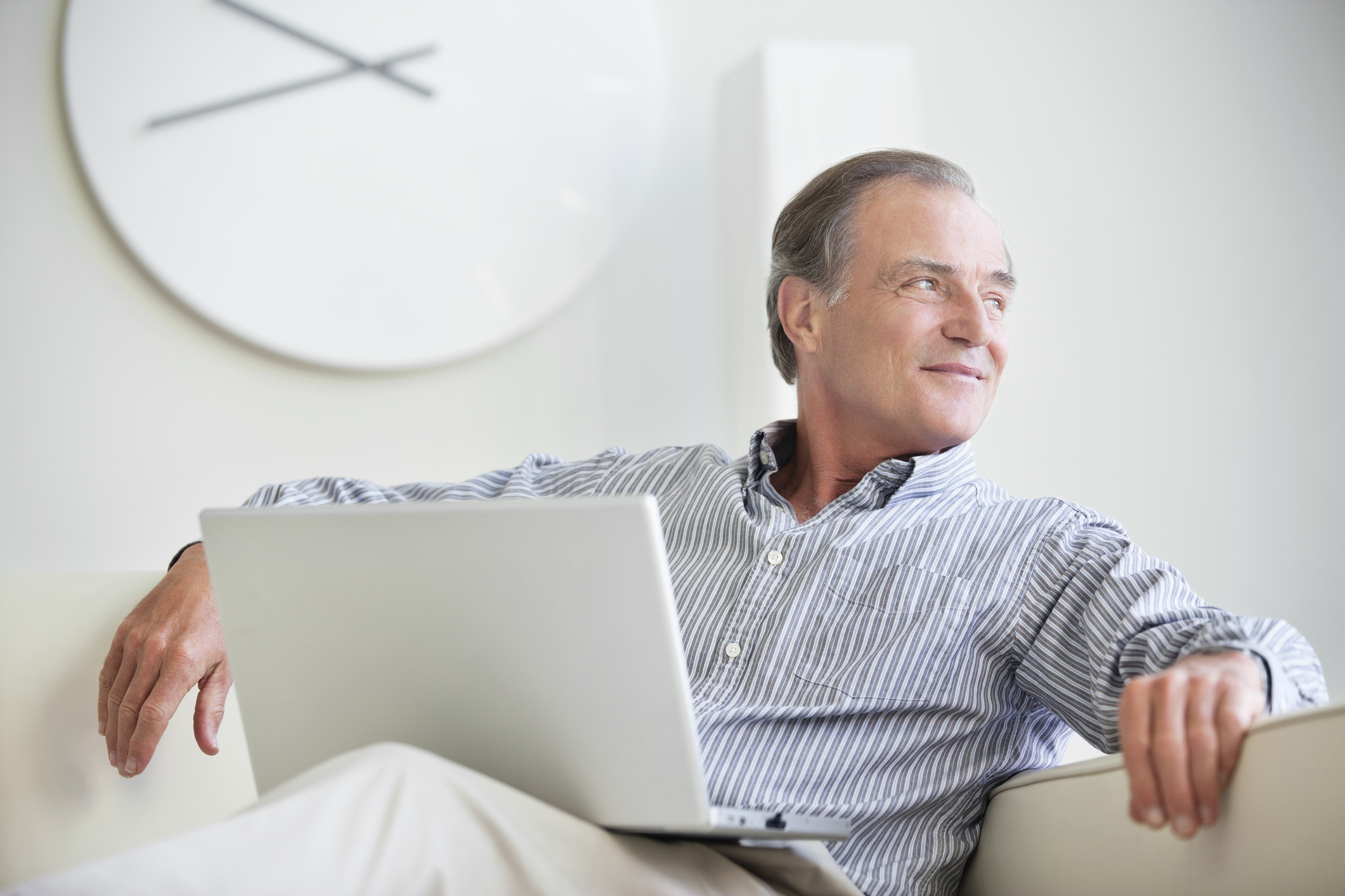 Man sitting on a couch looking out a window with a laptop on his lap