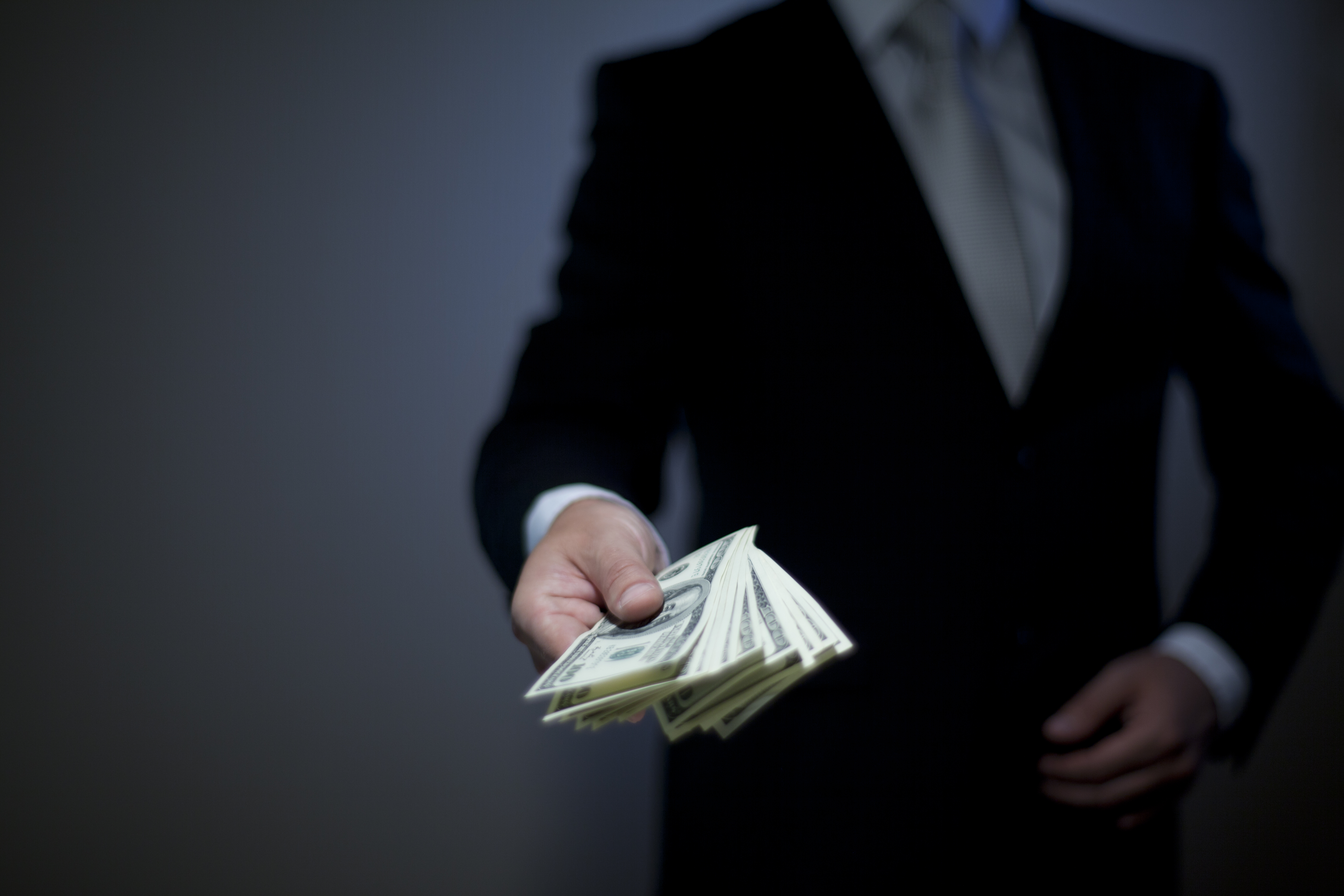 A person in a suit handing over a stack of cash.