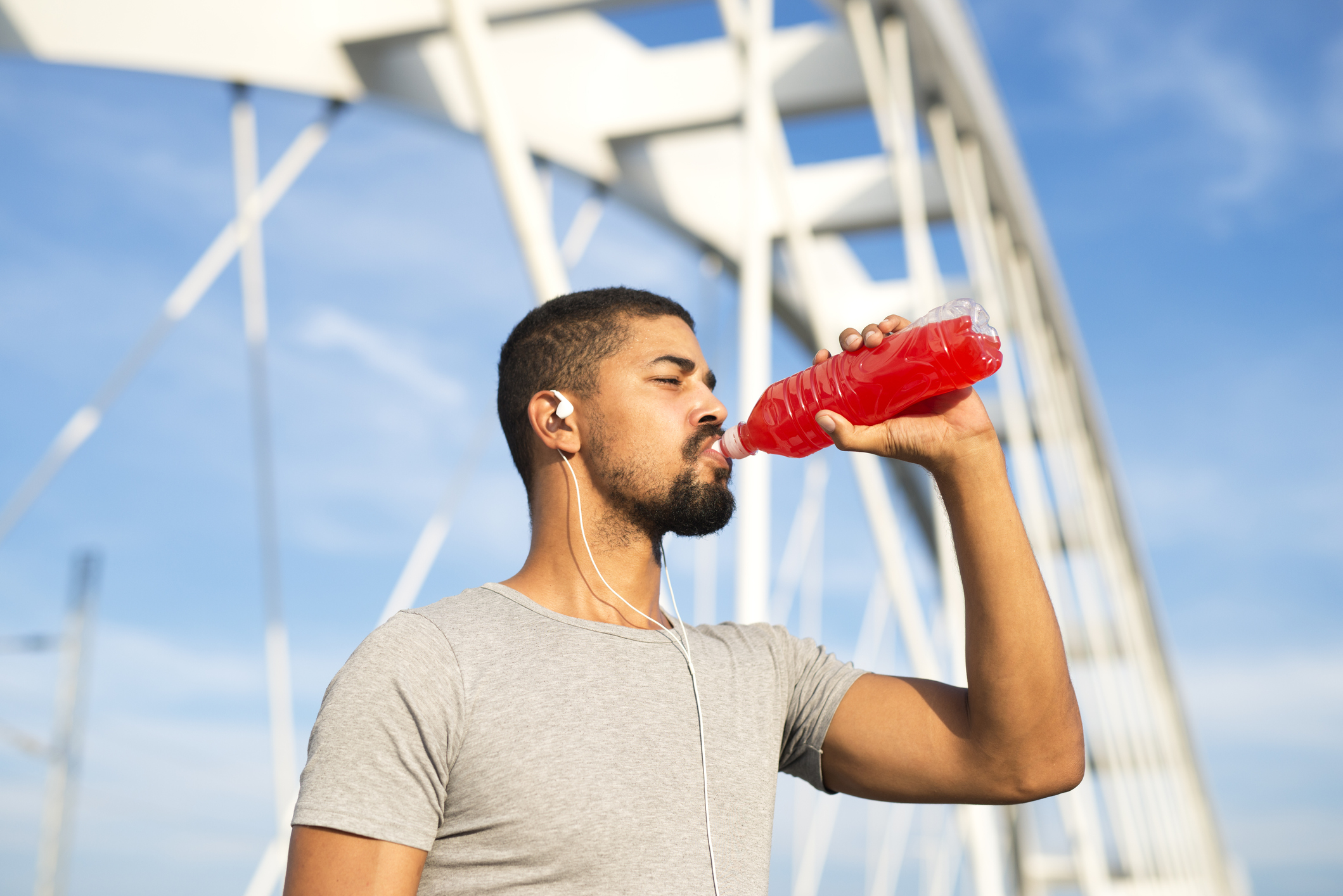 Man drinking red energy drink while standing beside bridge