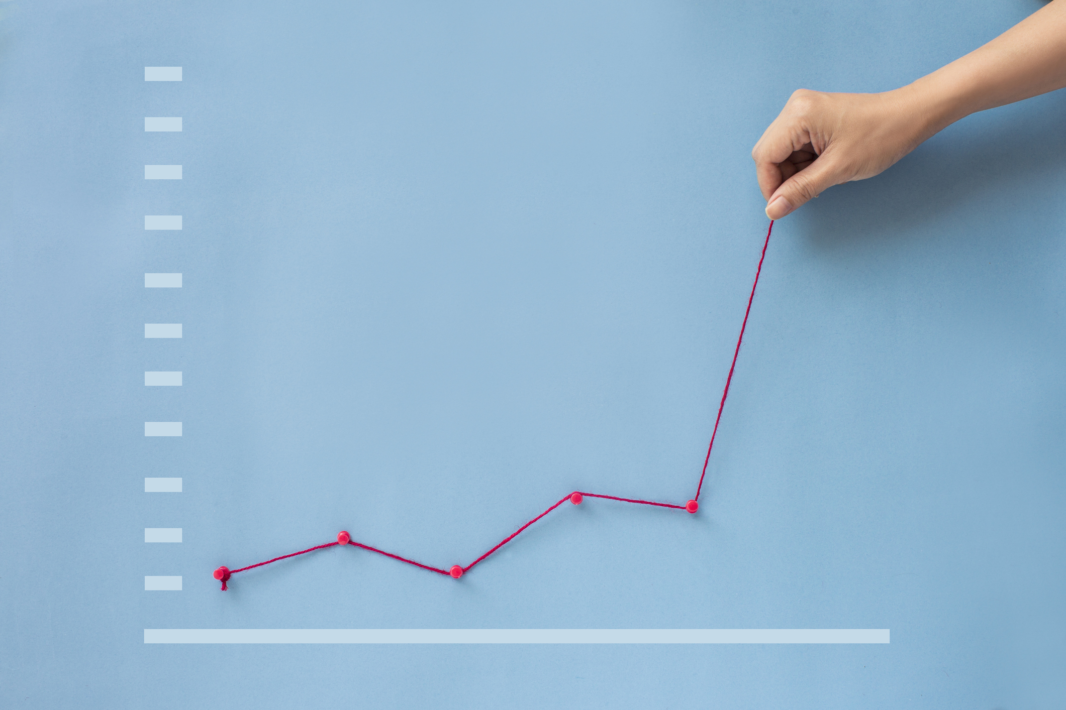 A graph, constructed of red yarn and set against a blue background, showing a rebounding trend.