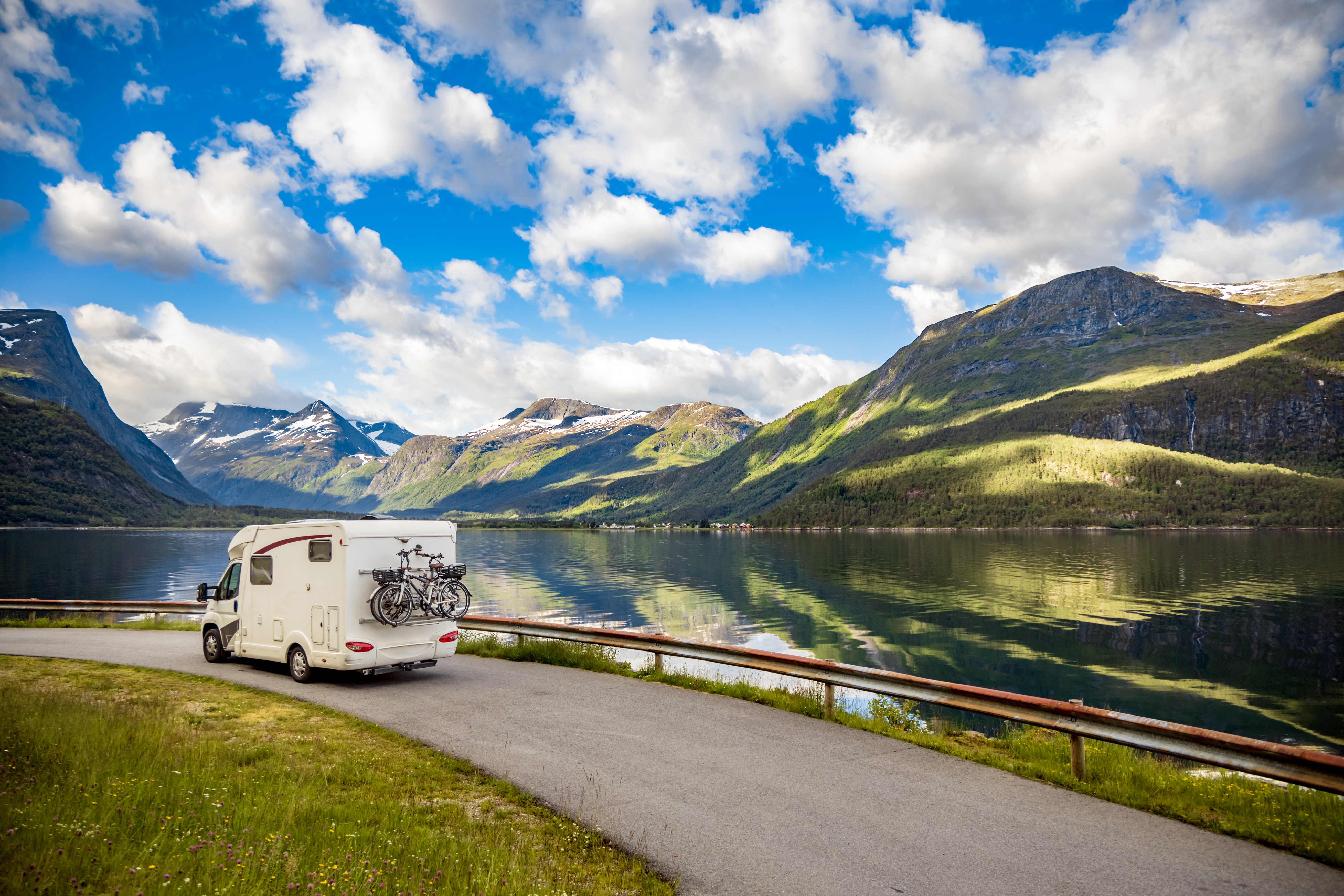 An RV on a road in front of mountains and a lake.