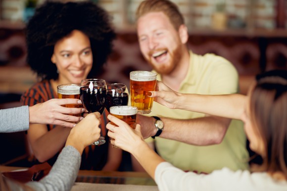 A group of young adults toasting with alcoholic beverages at a bar.