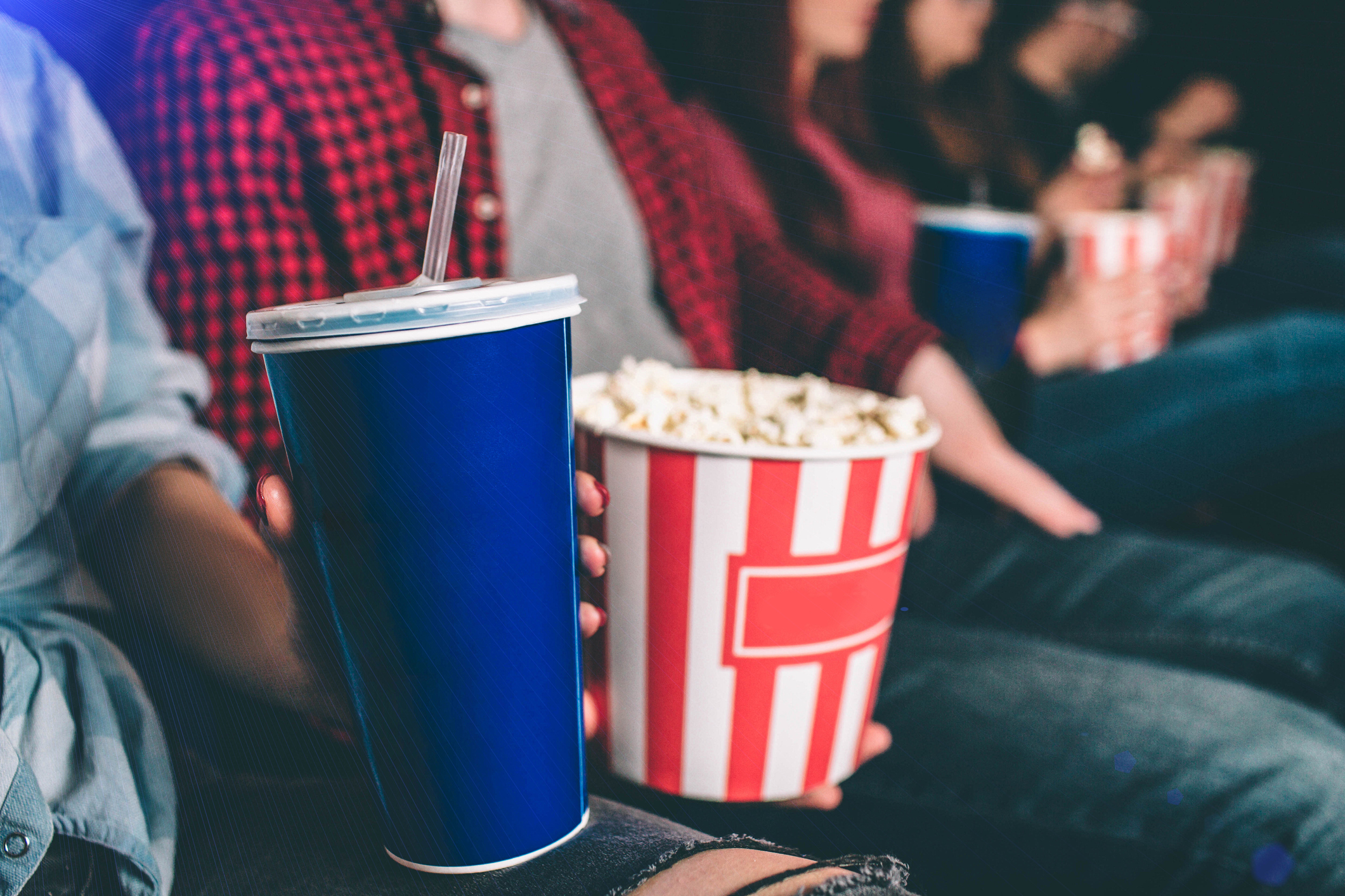 Patrons at a movie theater, one holding a bucket of popcorn and the other a soft drink.