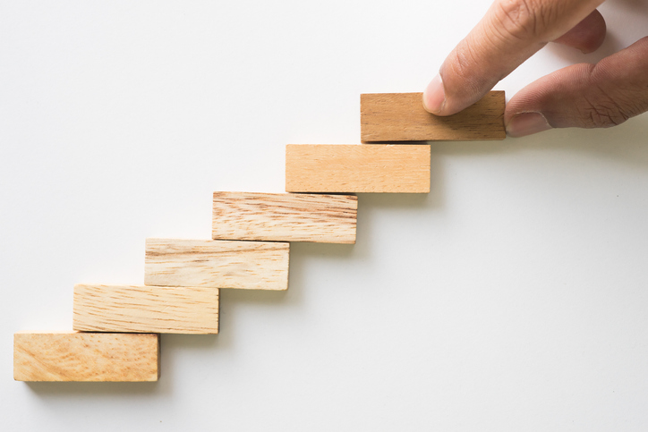 A hand placing blocks in an ascending stair pattern.