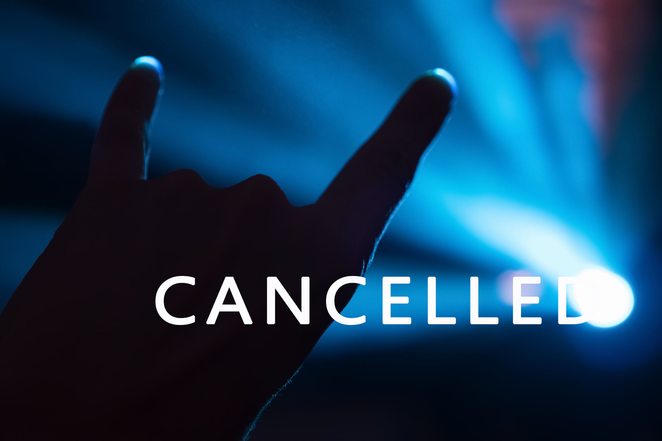 The word "cancelled" overlies a hand making "the devil's horns" rock concert gesture.