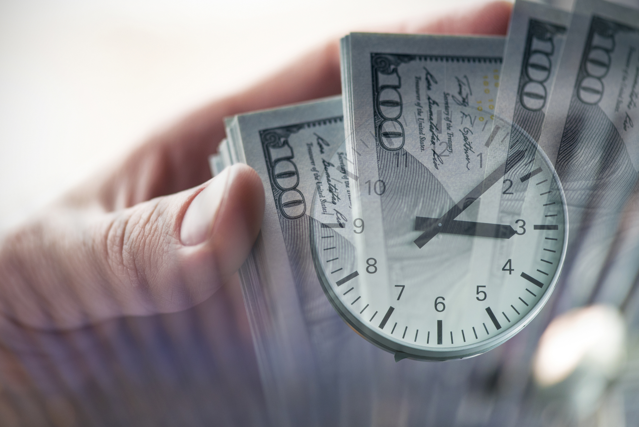 A clock superimposed atop a fanned pile of cash in someone's hands.