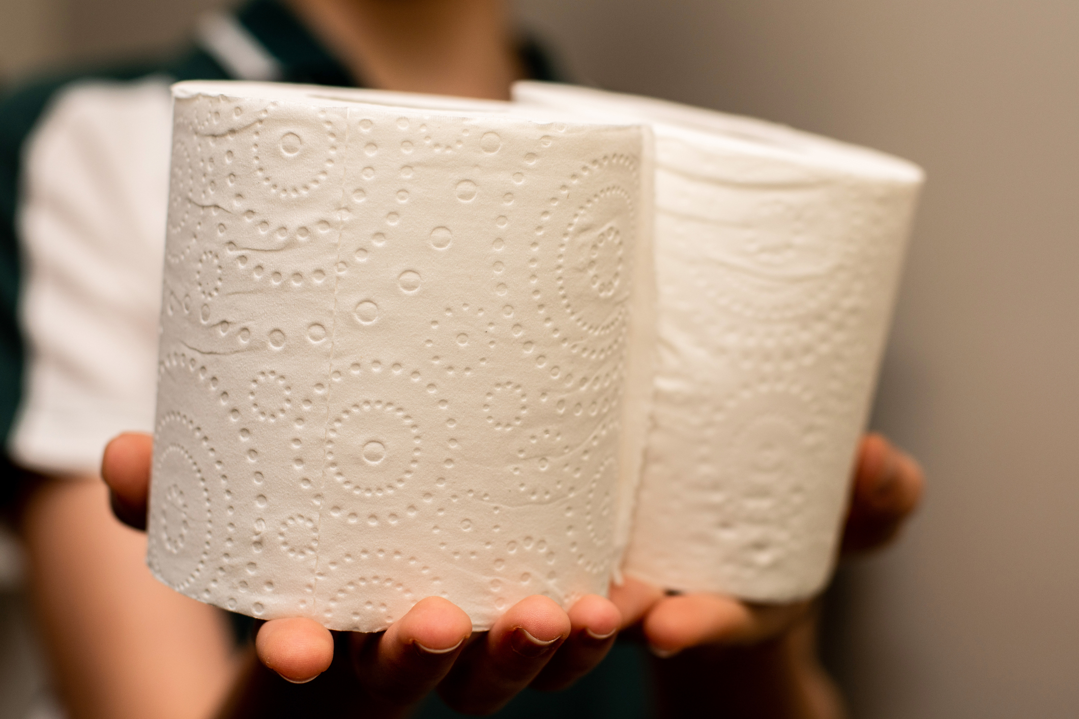 A woman holds two rolls of toilet paper.