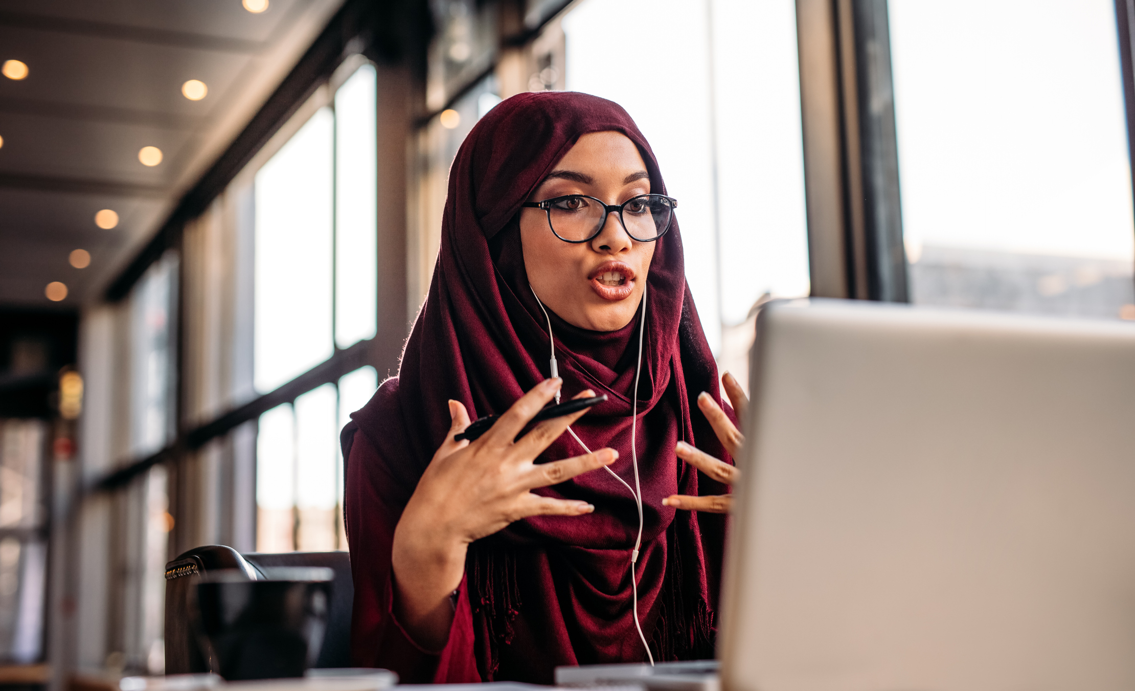 A woman talking and gesturing in front of her laptop.