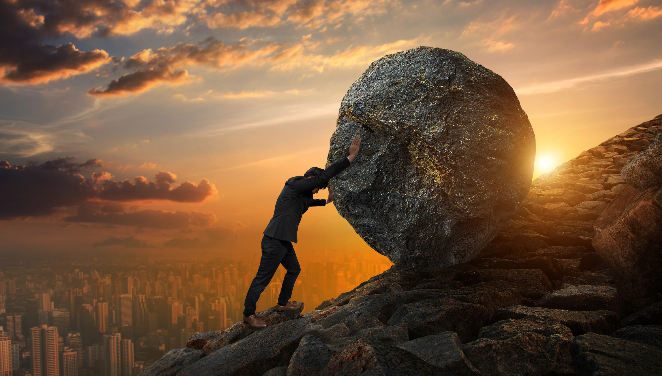 A businessman pushes a boulder uphill.