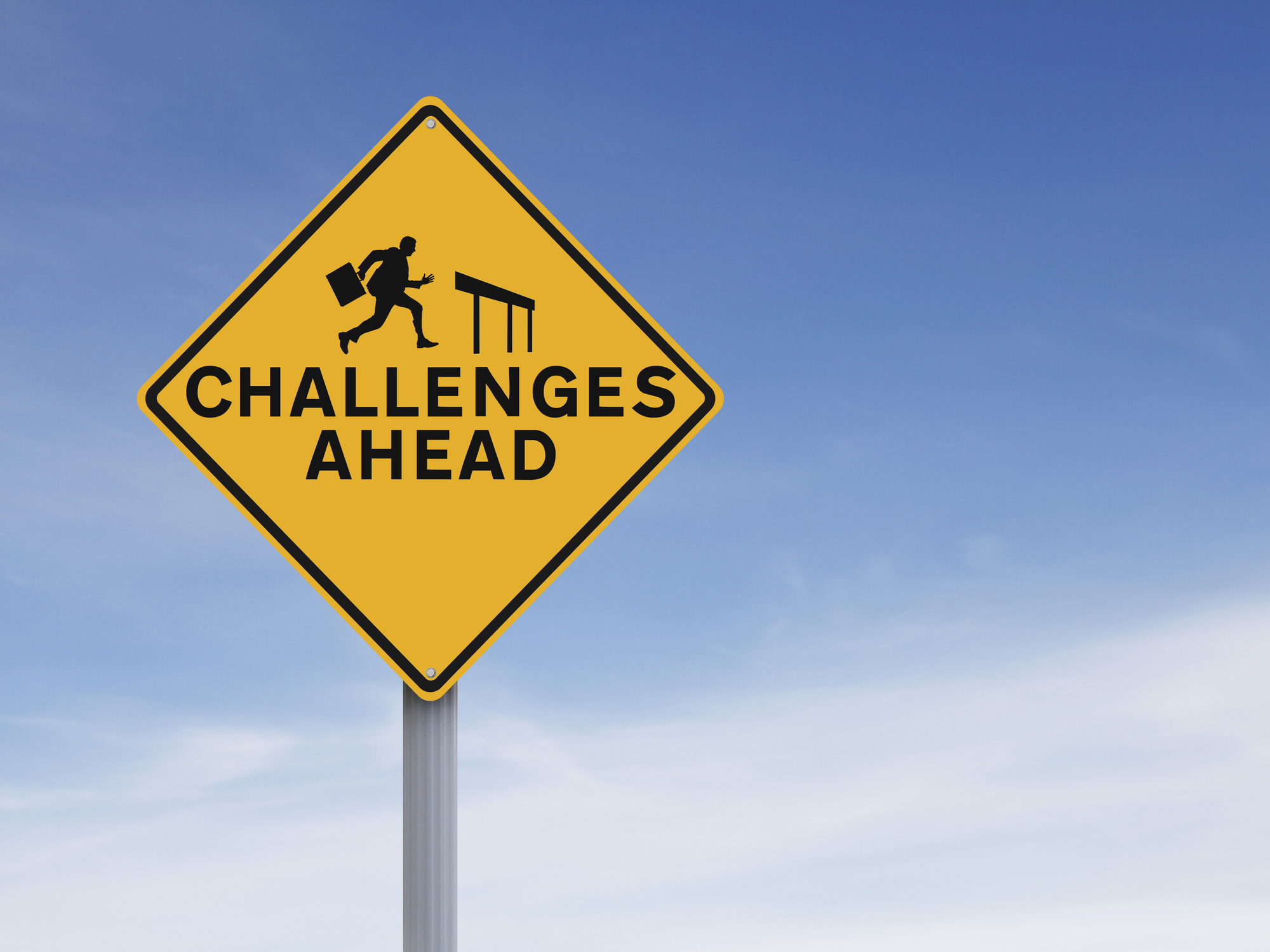 A road sign shows a business person approaching a hurdle and has the words challenges ahead.
