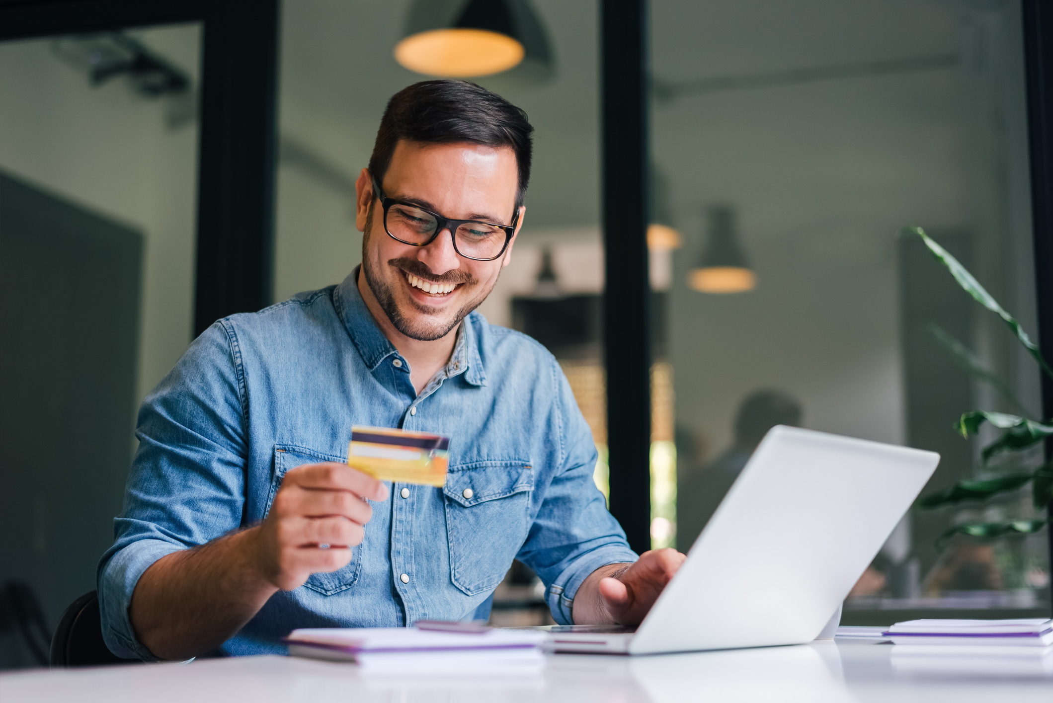 A young man smiles at his credit card while on his laptop.