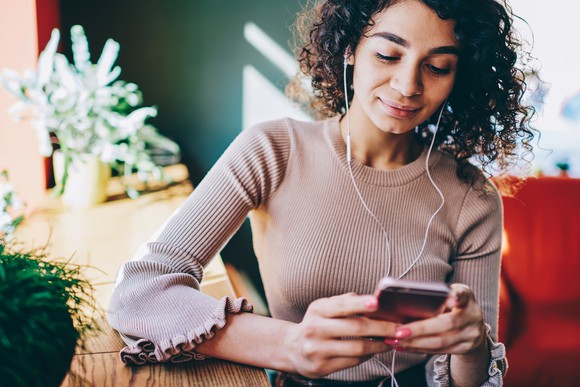 A young woman wearing headphones looking at her smartphone.