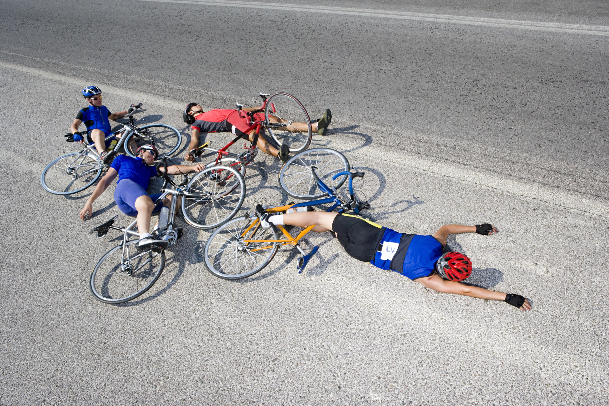 Four bicyclists who have crashed, lying in the road.