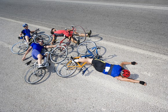 Four bicyclists who have crashed, lying in the road. 