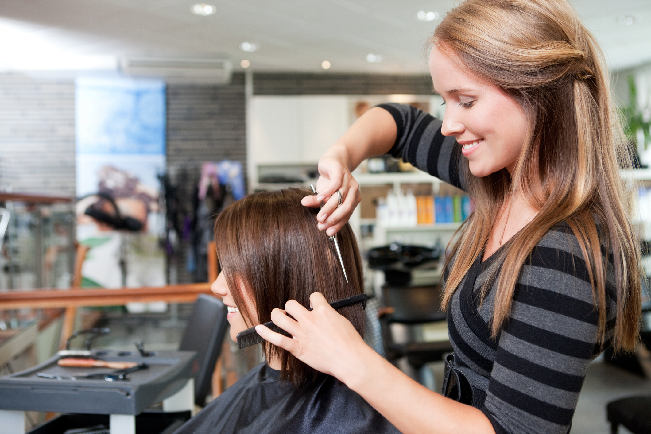 A woman cuts another woman's hair in a salon setting