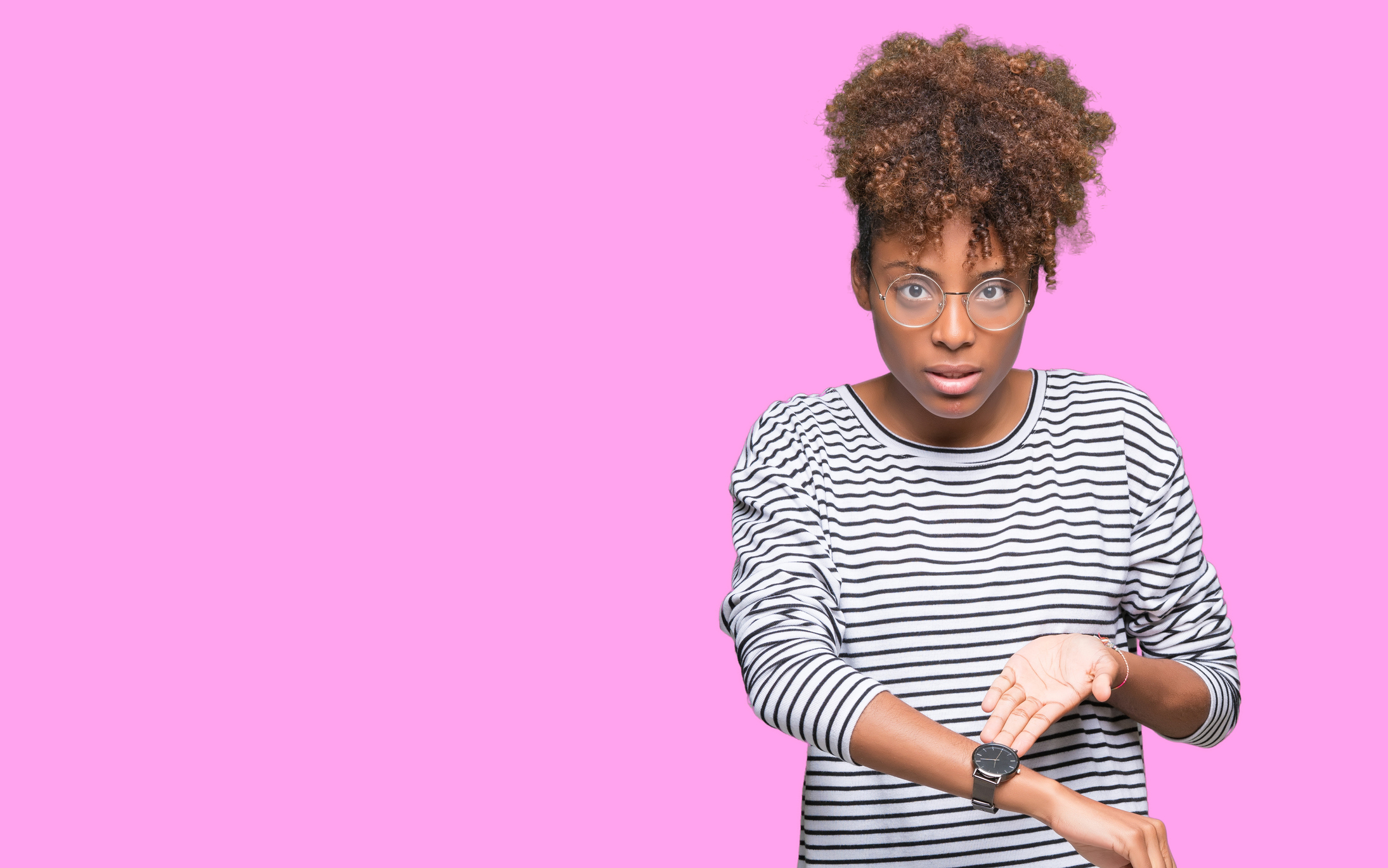 Young woman gesturing at her wristwatch with impatient expression.