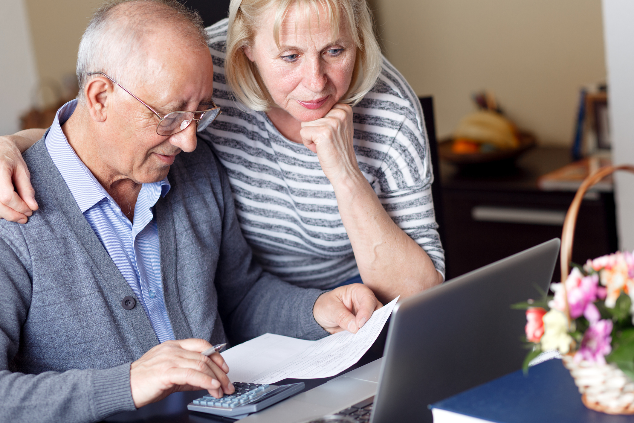 Older couple using a calculator while looking at a laptop. 